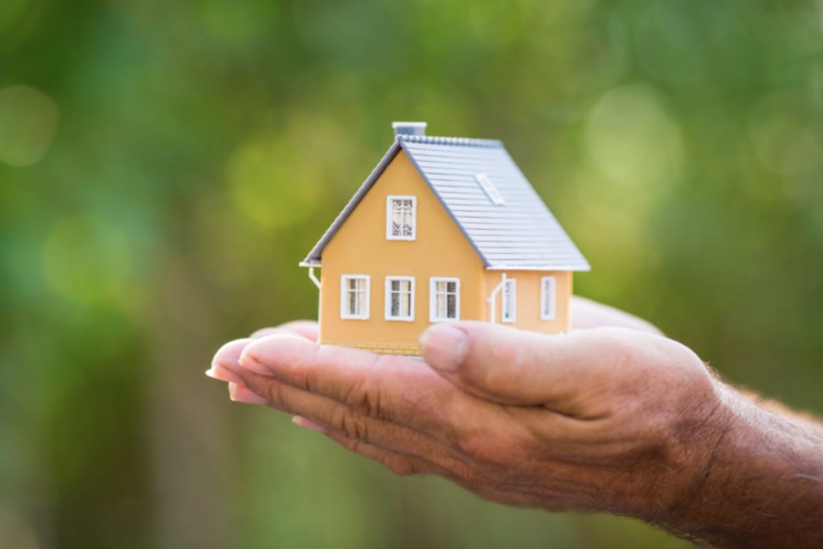 Modellino di casa tra le mani su sfondo naturale